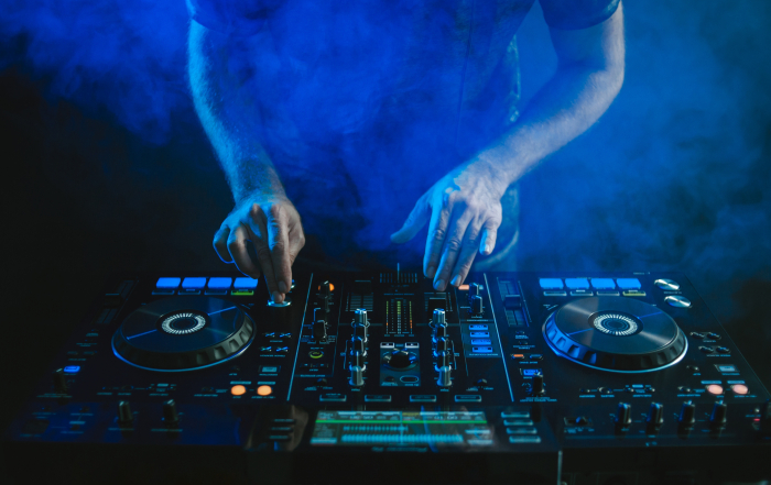A closeup of a DJ working under the blue lights against a dark background in a studio