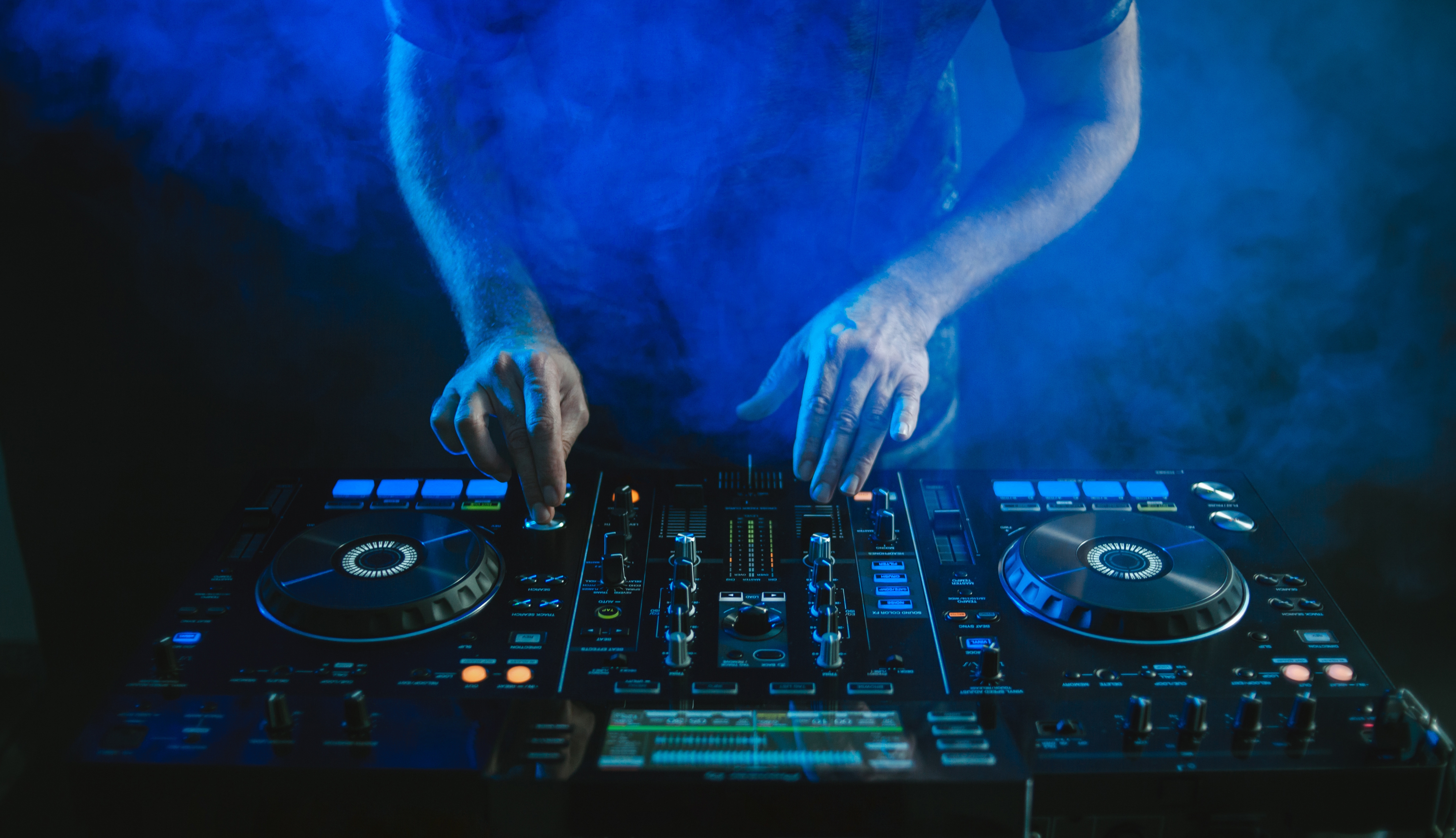 A closeup of a DJ working under the blue lights against a dark background in a studio