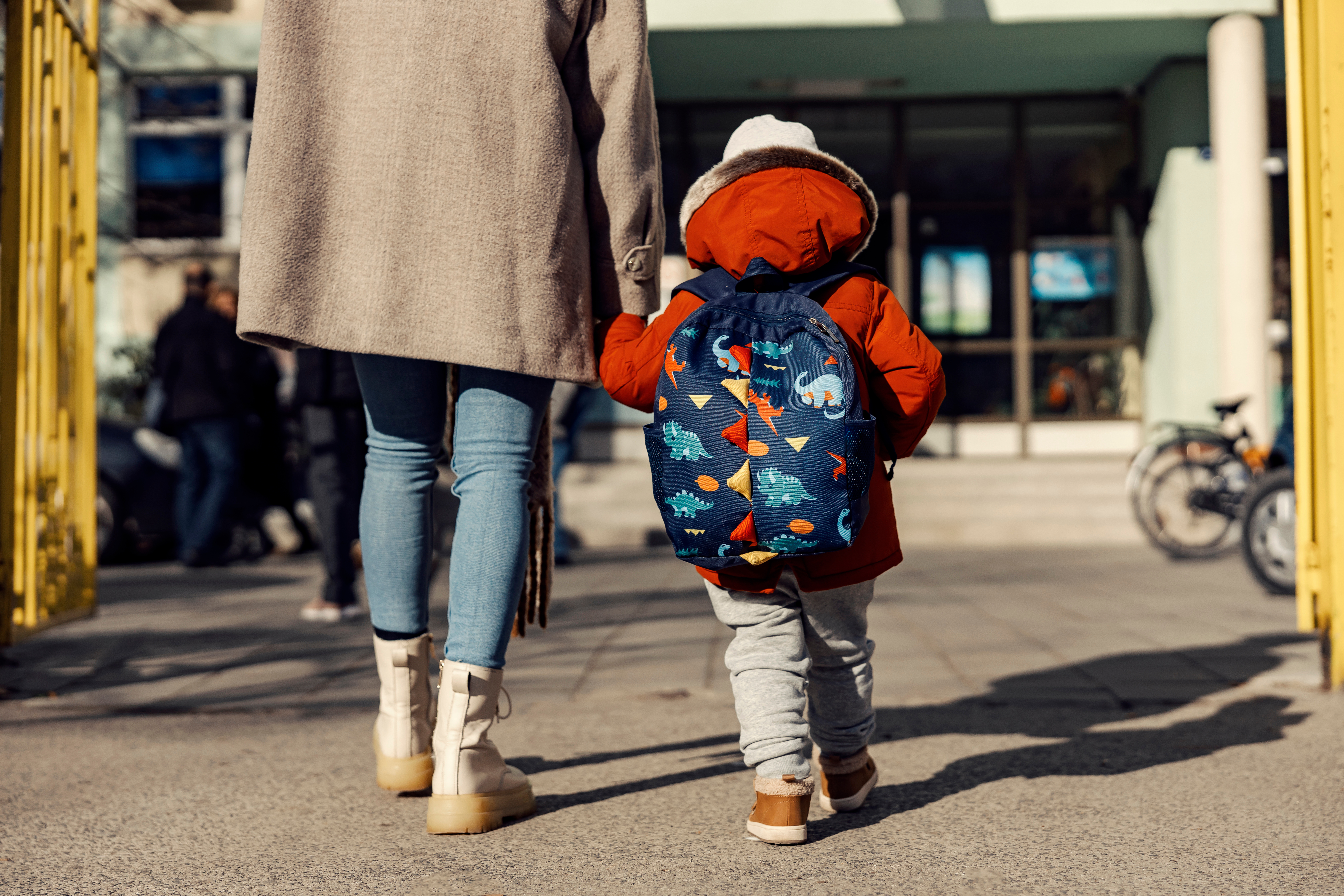 A mother entering the kindergarten yard with her preschooler boy.