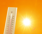 Thermometer showing high temperature against orange sky with bright sun. Extremely hot weather
