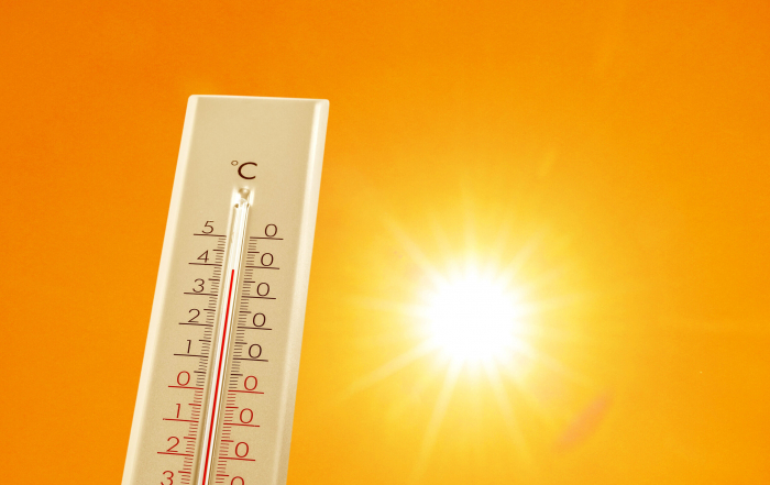 Thermometer showing high temperature against orange sky with bright sun. Extremely hot weather